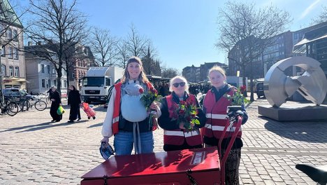 Das Bild zeigt drei Personen, die Rosen in den Händen halten.